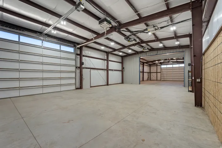 Expansive concrete flooring with high ceilings, multiple overhead garage doors, and exposed structural beams