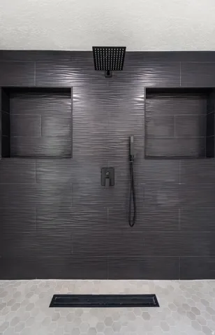 Textured dark gray tile shower surround with two recessed niches, a matte black rainfall shower head, and a linear drain
