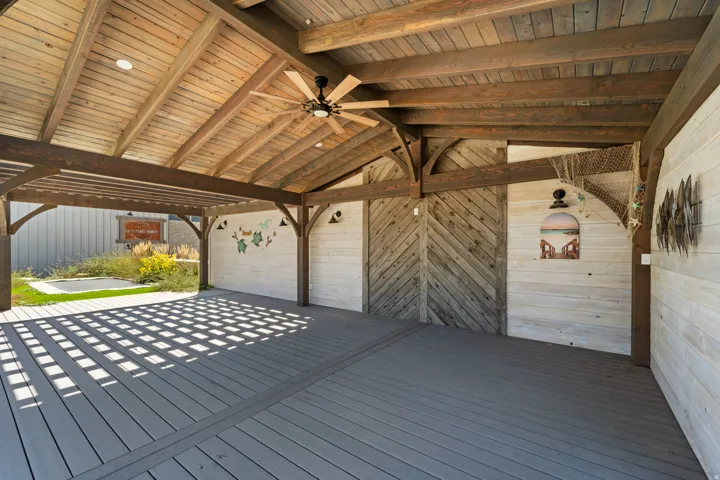 Expansive covered outdoor living area featuring a wood-finish ceiling, exposed wood beams, ceiling fan, and composite decking