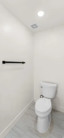 Recessed ceiling lighting, ceiling-mounted exhaust fan, white walls, black towel bar, and light-toned flooring