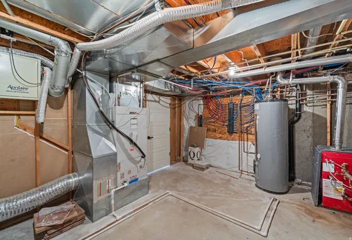 Concrete flooring with exposed ceiling joists, comprehensive ductwork, water heater, and mechanical systems
