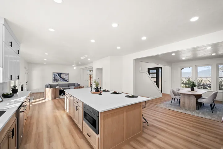 Open-concept living area with wood-finish flooring, recessed lighting, a kitchen island with integrated microwave, and white cabinetry with dark hardware