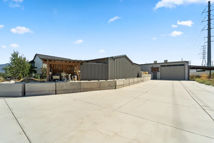 Expansive concrete driveway, a dedicated utility area with a wooden pergola, a large corrugated metal building, and a separate structure with a roll-up garage door