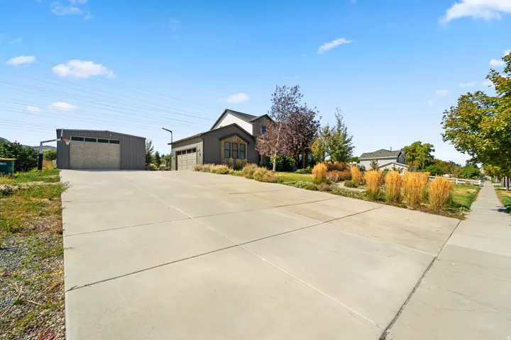 Expansive concrete driveway, detached garage with a basketball hoop, attached garage, and mature landscaping with ornamental grasses