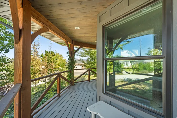 Covered exterior porch featuring wood beams and railing, plank decking, and a large window with trim