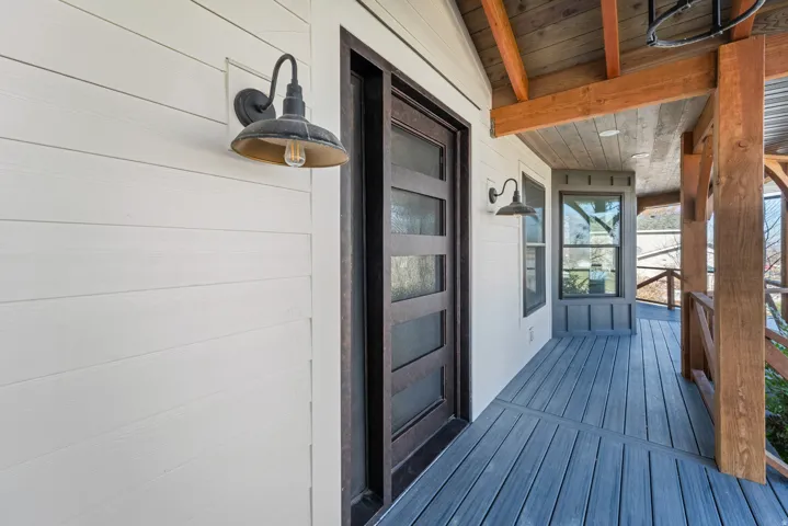 Covered porch with composite decking, industrial-style pendant lighting, and black-framed glass door entry