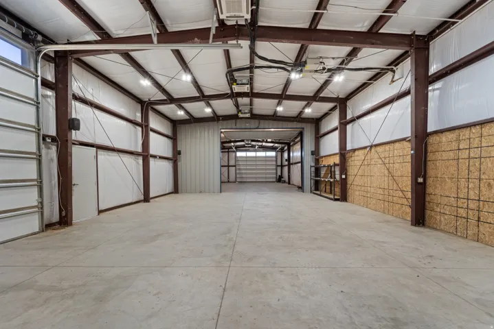 Expansive warehouse space featuring a concrete floor, exposed structural beams, insulated walls, overhead lighting, and multiple roll-up doors