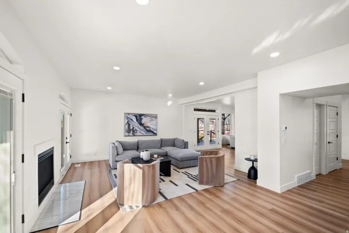 Spacious living area featuring wood-finish flooring, recessed lighting, and a fireplace with a stone-finish hearth