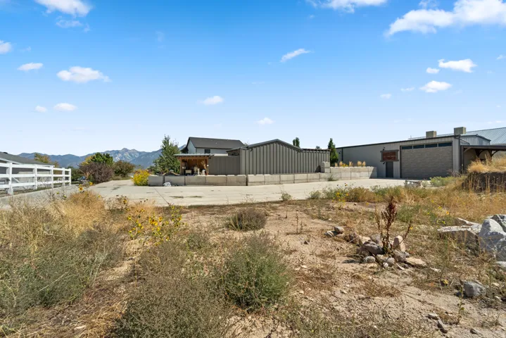 Gated property entrance with a white fence, featuring a large concrete-paved area and mountains in the background
