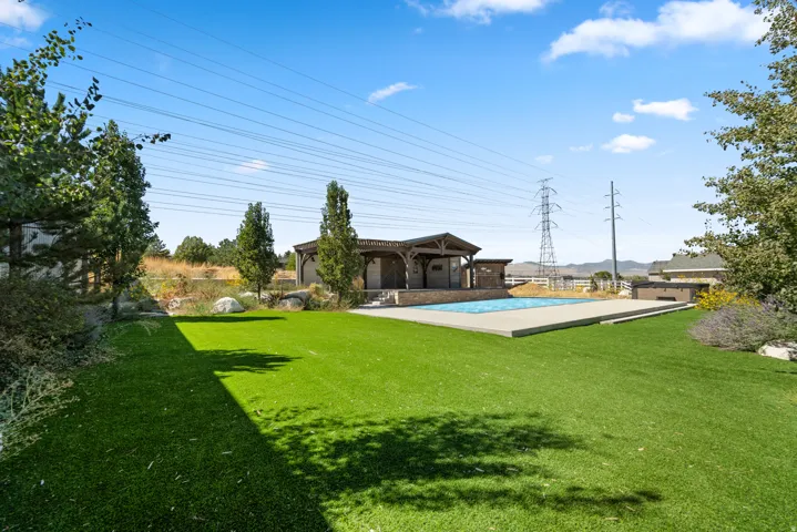 Expansive turf lawn with an in-ground swimming pool, stone-clad pool house, concrete pool decking, and mature landscaping