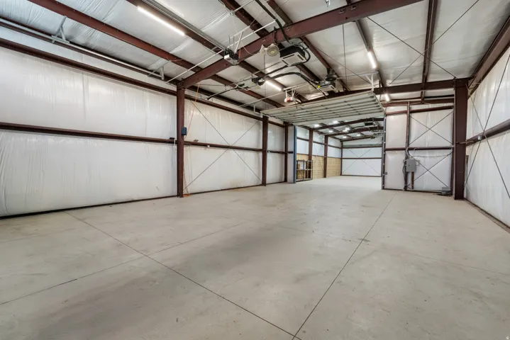 Spacious concrete flooring with exposed structural beams, high ceilings, bright overhead lighting, and an overhead door