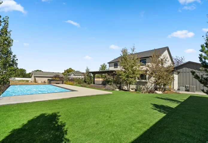 Expansive yard with a rectangular swimming pool, concrete pool deck, and a wooden pergola structure