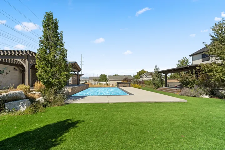 Expansive green space featuring a rectangular swimming pool with surrounding concrete patio