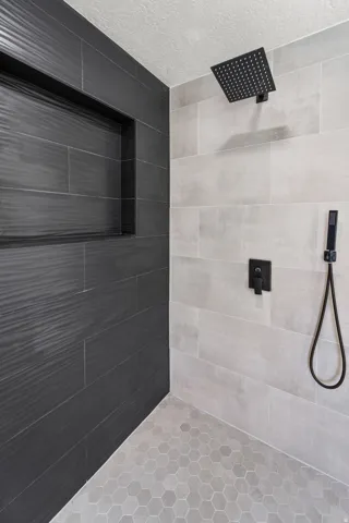 Shower featuring a built-in niche, matte black shower fixtures, light gray hexagonal floor tiles, and large format wall tiles in contrasting tones