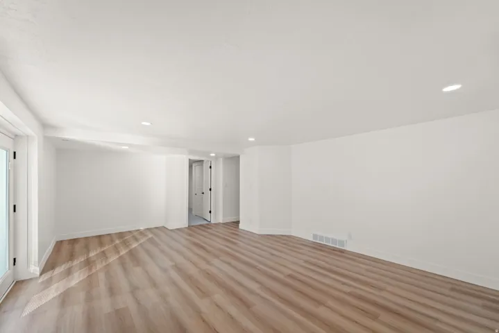 Spacious room featuring wood-finish flooring, recessed lighting, and a white color palette