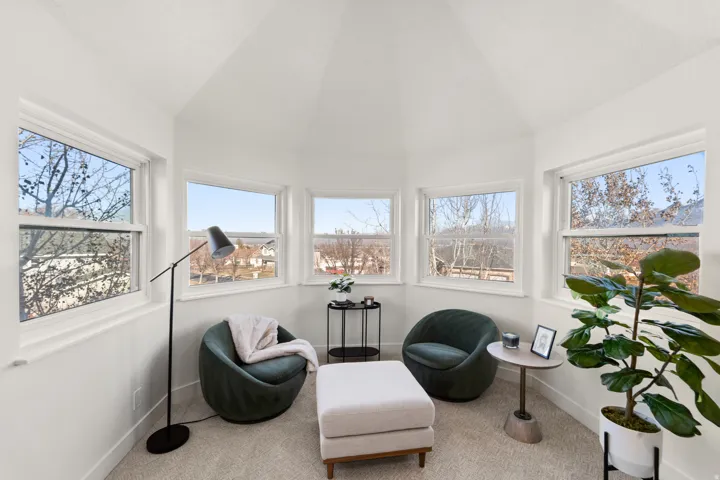 Angled room with multiple large windows, white walls, and light-colored carpeting