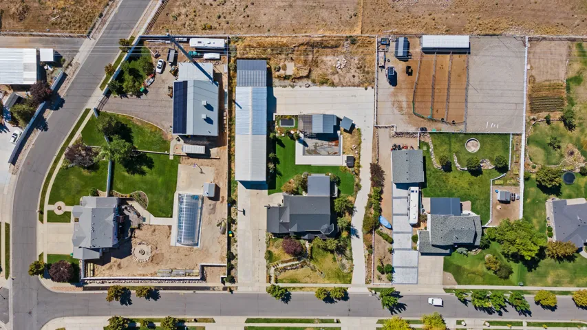 Aerial perspective showcasing multiple properties with extensive paved and unpaved areas, mature landscaping, and an inground swimming pool