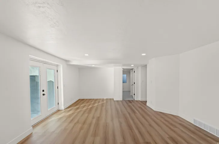 Recessed lighting, wood-finish flooring, white walls, and white French doors with dark hardware