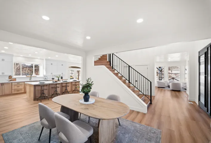 Open-concept living space featuring wood-finish flooring, a kitchen with an island, a dining area, and a staircase with black railings