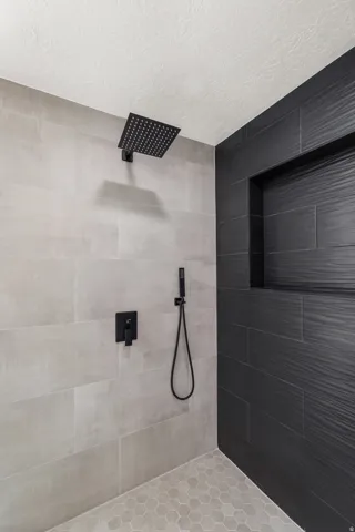 Walk-in shower featuring a matte black rain shower head, matte black handheld shower, and a matte black control panel