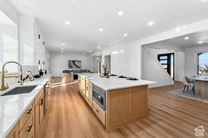 Bright kitchen featuring a large central island, light wood-finish flooring, white cabinetry, and recessed lighting