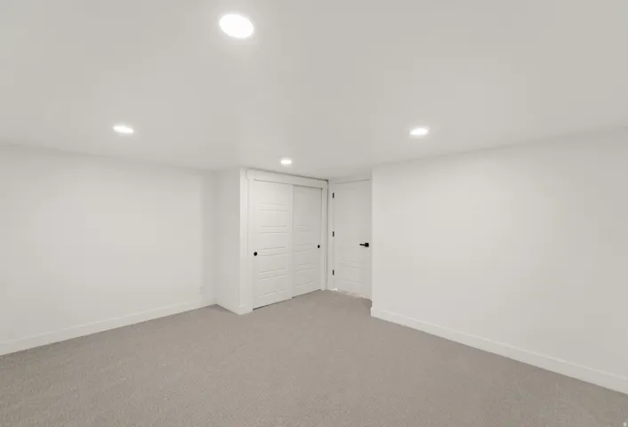 Recessed lighting illuminates neutral-toned carpeting and bright white walls