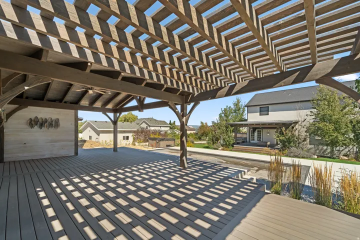 Expansive outdoor decking with a large pergola structure, featuring a built-in ceiling fan and an integrated accent wall