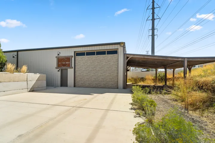 Metal-sided structure with a large garage door, concrete drive, and an attached wood-frame covered area