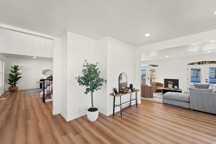 Wood-finish flooring throughout, white walls, recessed ceiling lighting, and a fireplace with a white mantel