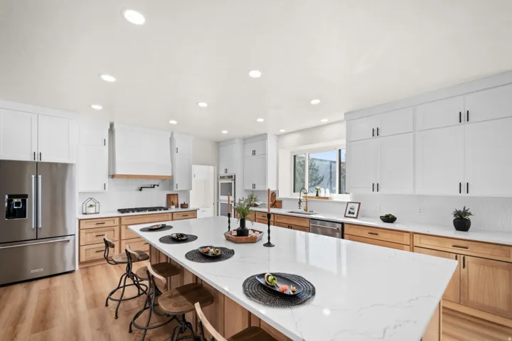 Spacious kitchen featuring an expansive island with seating, stainless steel appliances, wood-finish flooring, white upper cabinetry, and wood-tone lower cabinetry