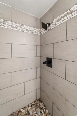 Shower stall featuring large format tile walls, a decorative mosaic tile accent band, a river rock floor, and matte black fixtures