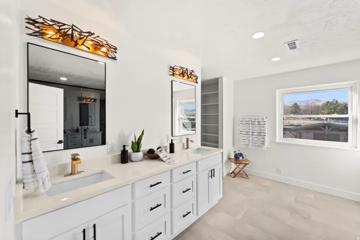 Double vanity with white cabinetry and light-toned countertops, featuring rectangular undermount sinks and modern gold-toned faucets