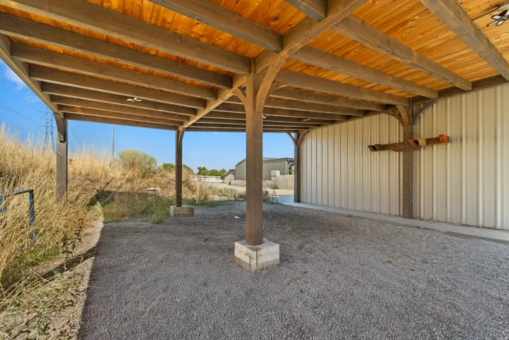 Covered outdoor structure with exposed wood beams, finished wood ceiling, and gravel flooring