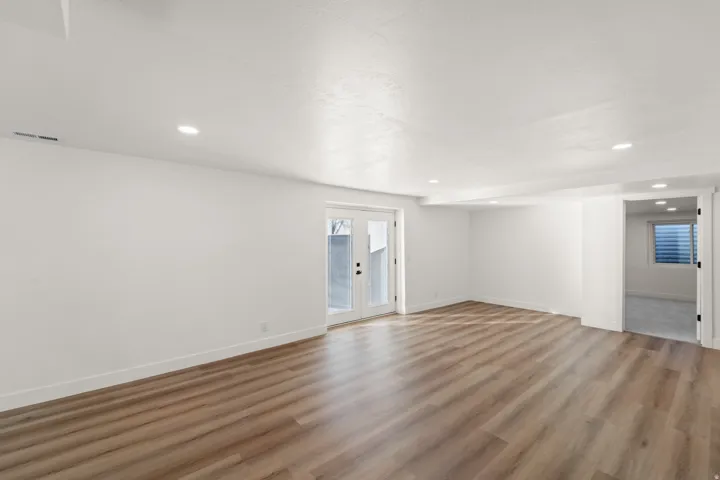 Spacious room featuring wood-finish flooring, white walls, recessed lighting, and white French doors