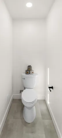Recessed lighting, white toilet, matte black toilet paper holder, light gray floor tiling, and white wall finishes