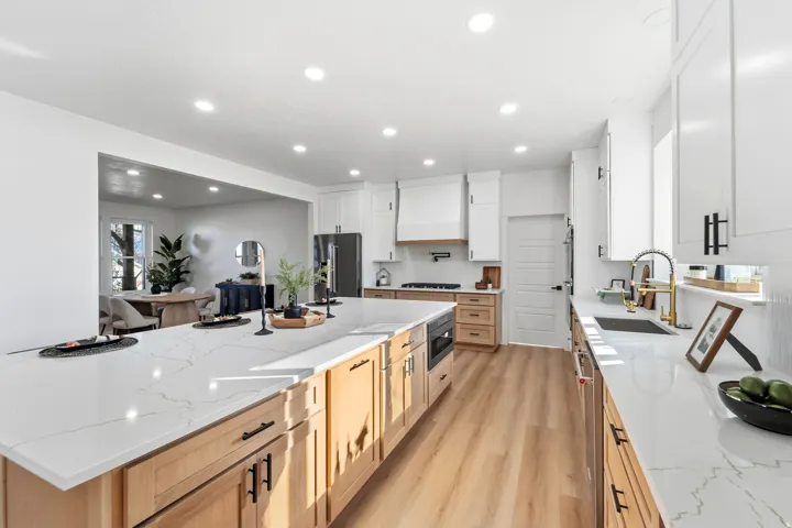 Spacious kitchen featuring an expansive island with a quartz countertop, wood-finish flooring, white cabinetry, and stainless steel appliances