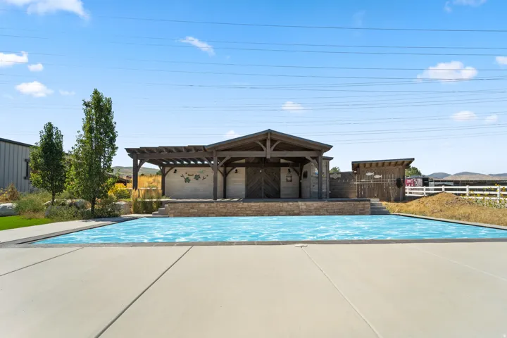 Expansive outdoor pool area featuring a pergola-covered structure, a separate utility shed, and a surrounding concrete patio