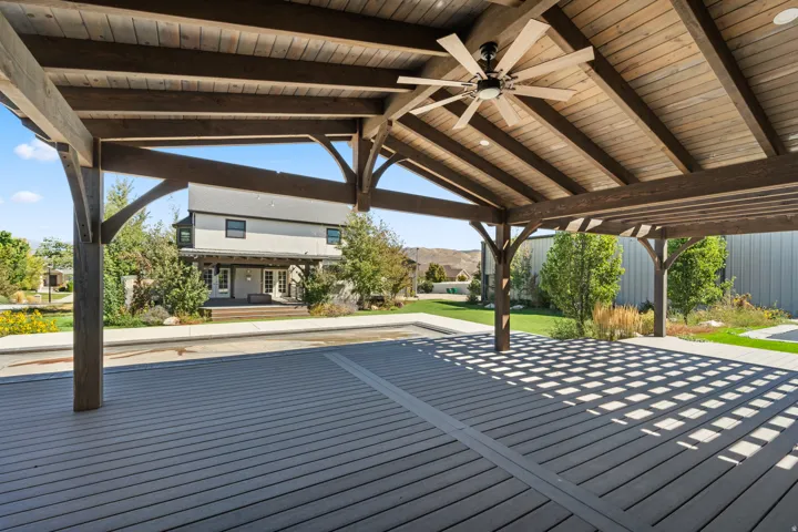 Expansive outdoor deck featuring a wood-finish pergola with a ceiling fan, composite decking, and a manicured lawn