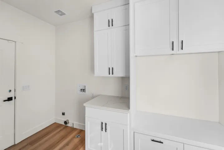 White shaker cabinetry with black hardware, wood-finish flooring, and a stone-finish countertop