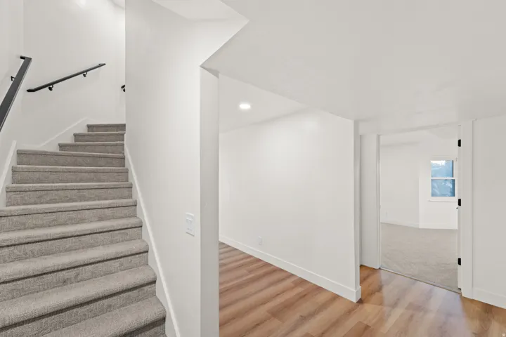 Carpeted staircase with black handrails, wood-finish flooring, and recessed ceiling lighting