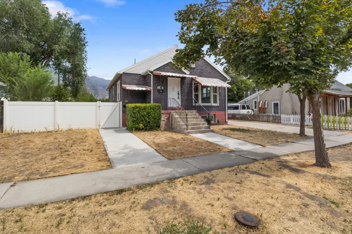 Brick exterior with a white vinyl fence and gate, concrete walkway, and mature trees