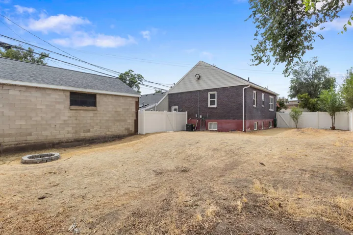 Expansive yard featuring a privacy fence, a detached auxiliary building with a shingle roof, and a built-in fire pit