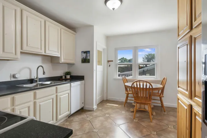 Kitchen featuring upper and lower cabinetry, dark countertops, a double basin sink, and tile flooring
