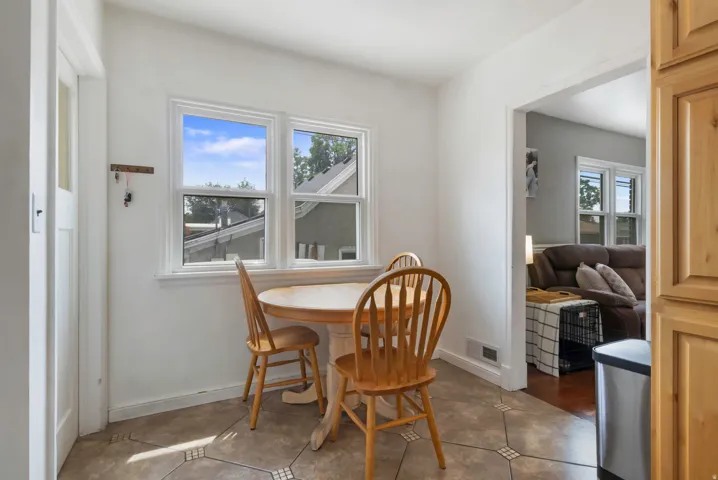 Bright corner office or den featuring dual windows with natural light, wood-finish flooring with geometric inlay detailing, and direct access to adjacent living spaces