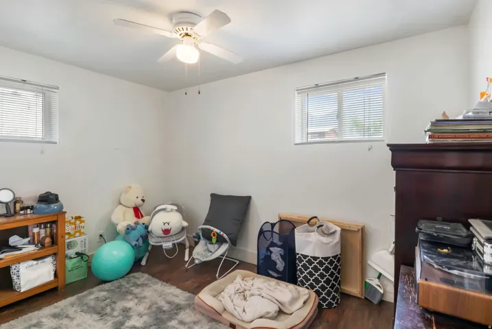 White walls, two windows with blinds, wood-finish flooring, and a ceiling fan with integrated lighting