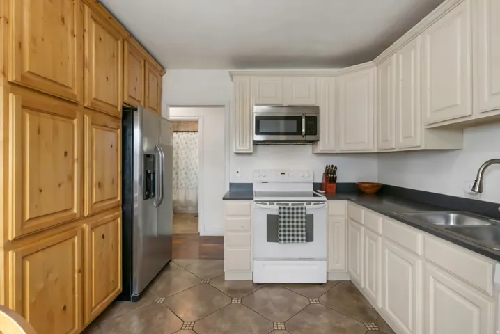 Stainless steel refrigerator, white cabinetry, dark countertops, built-in microwave, and patterned tile flooring