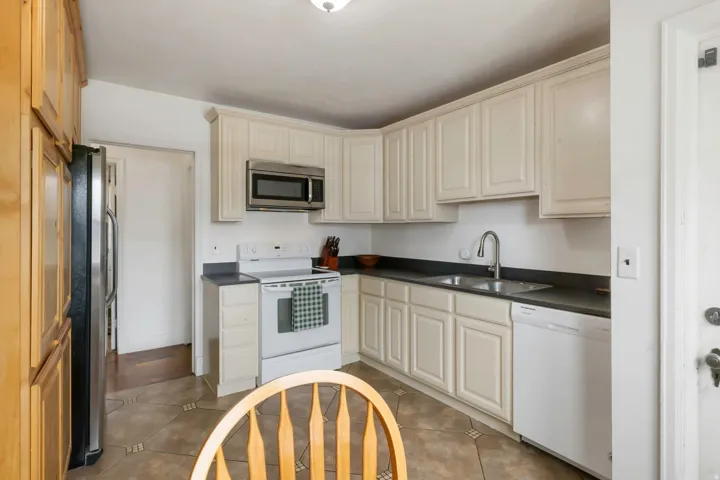 Kitchen featuring white cabinetry, dark countertops, stainless steel appliances, and patterned floor tiling