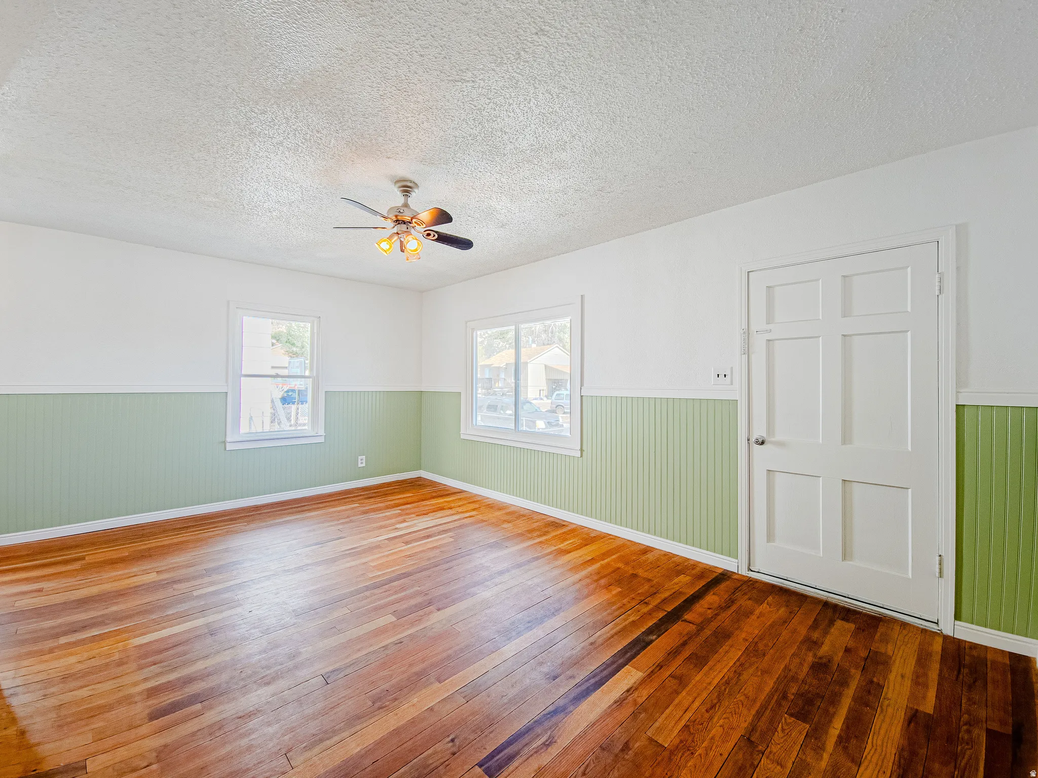 Hardwood flooring, painted beadboard wainscoting, white trim, multiple windows, and a ceiling fan with integrated lighting