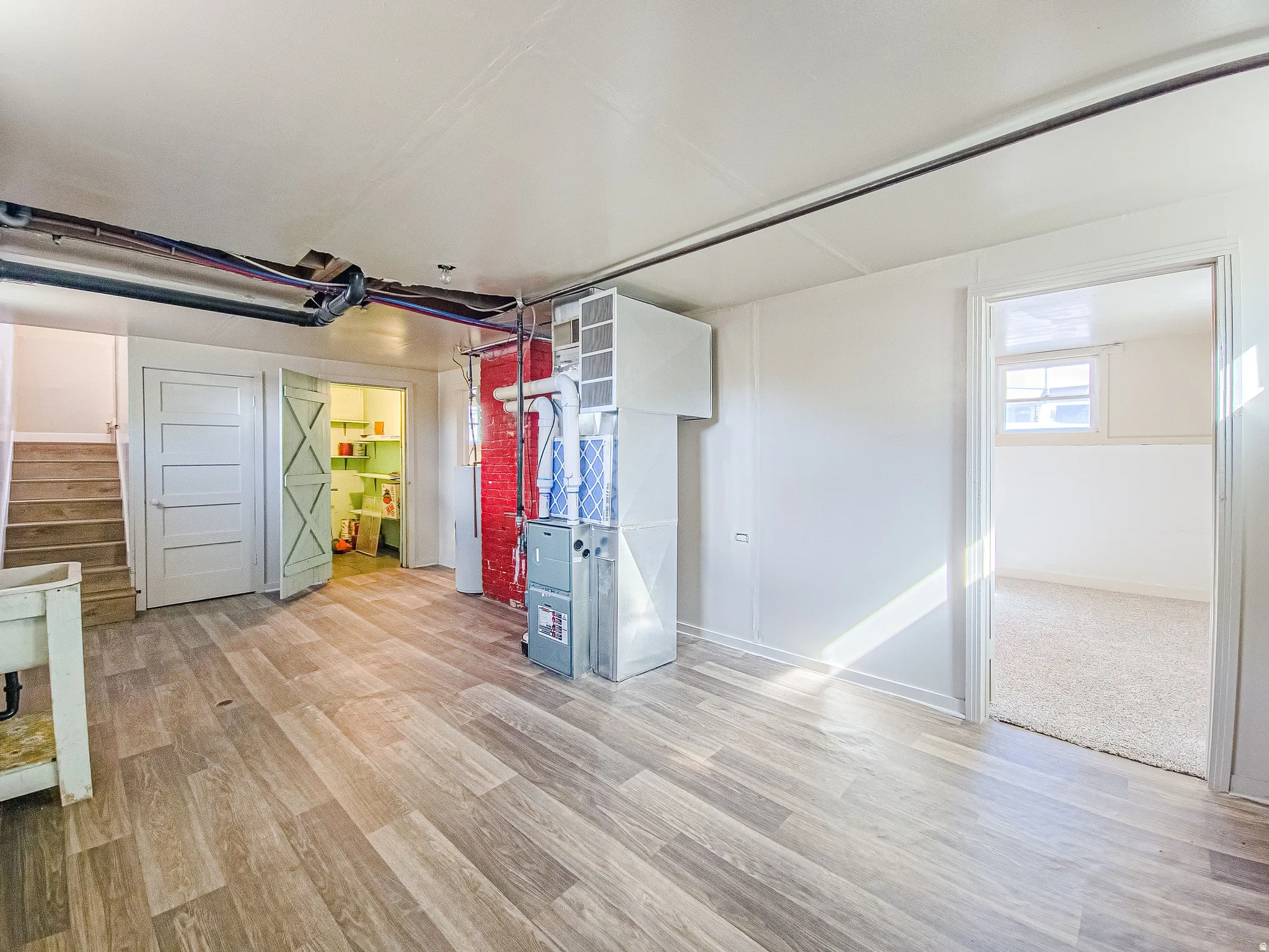 Wood-finish flooring with a utility sink, exposed ceiling pipes, and a window