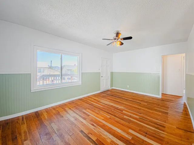 Hardwood flooring, beadboard wall paneling, white trim, ceiling fan light fixture, and window
